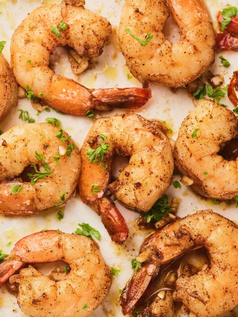 Close-up of cooked of garlic butter shrimp garnished with chopped parsley on a light surface.