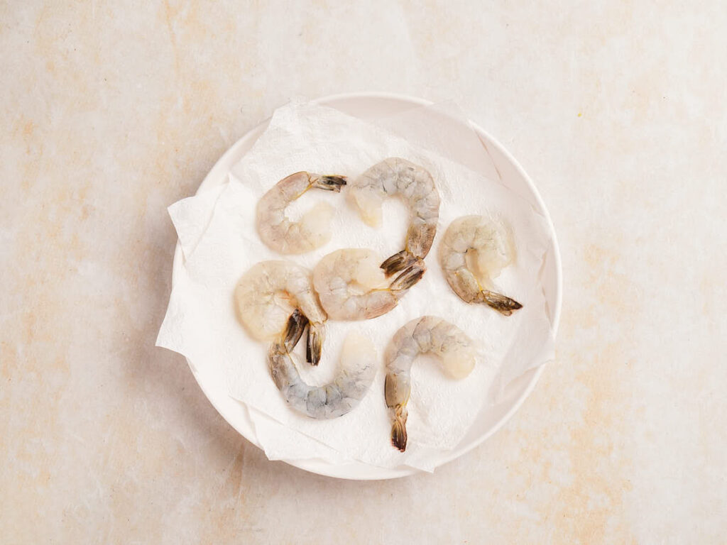 Raw, peeled shrimp arranged on a white paper towel in a white bowl.