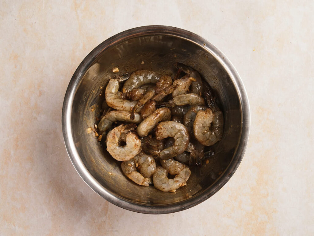 Raw shrimp marinated with spices and garlic in a stainless steel mixing bowl.
