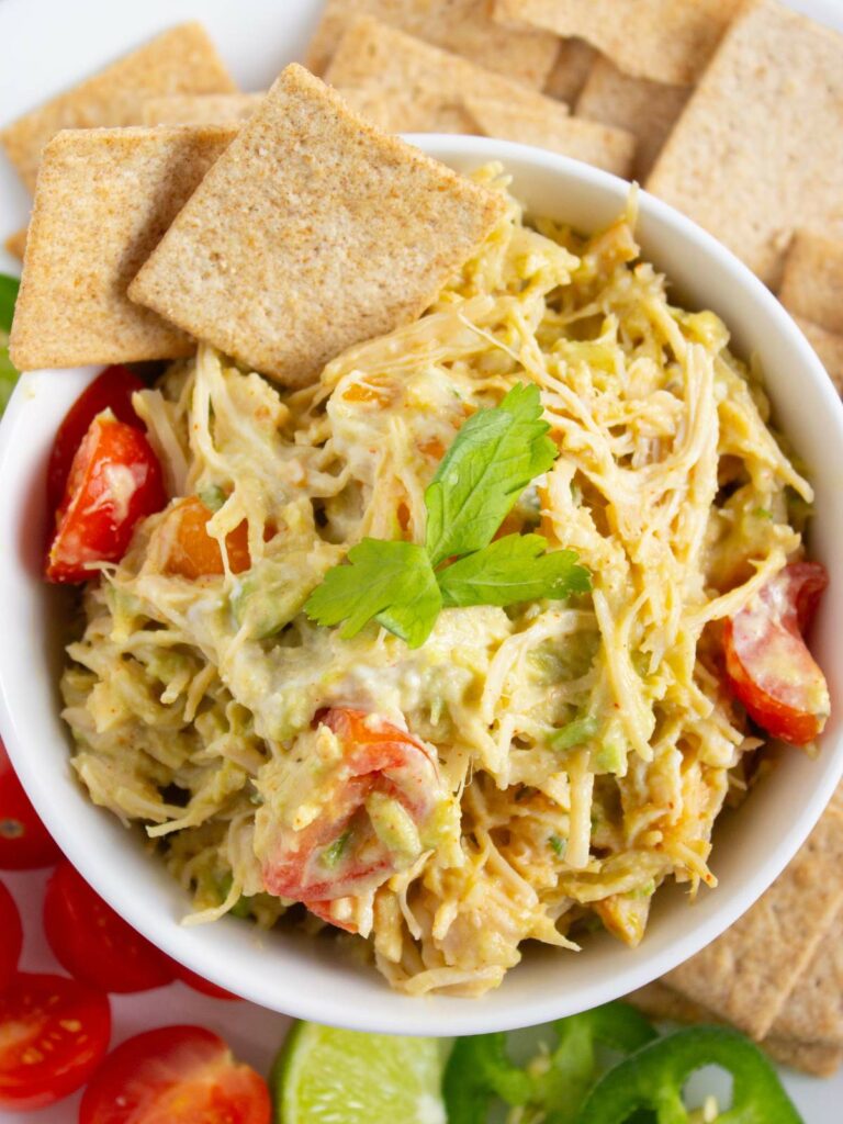 A bowl of healthy chicken salad with sliced cherry tomatoes, topped with cilantro.