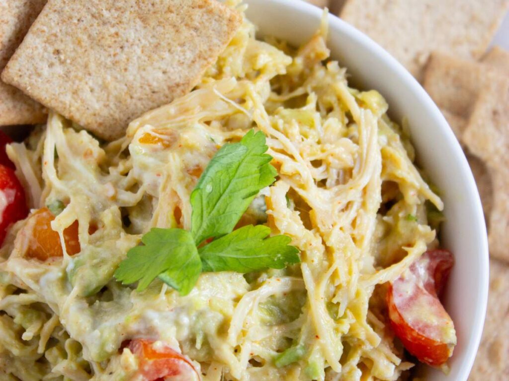 A healthy chicken salad mixed with avocado and cherry tomatoes, garnished with parsley.