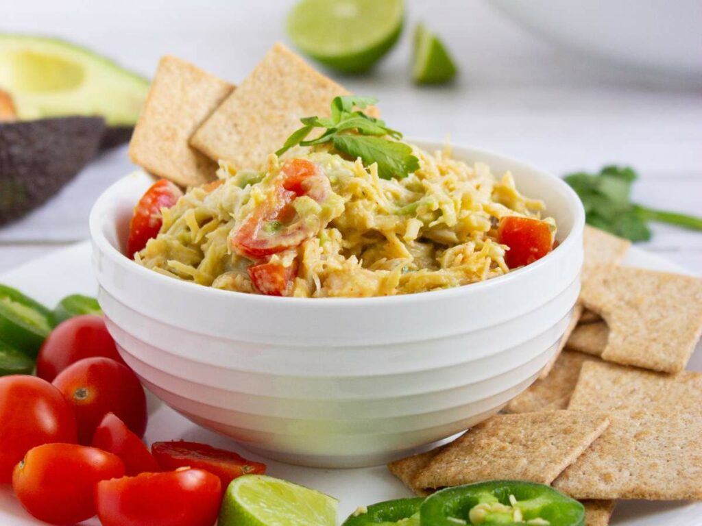 A bowl of healthy chicken salad with tomatoes and avocado, garnished with herbs.