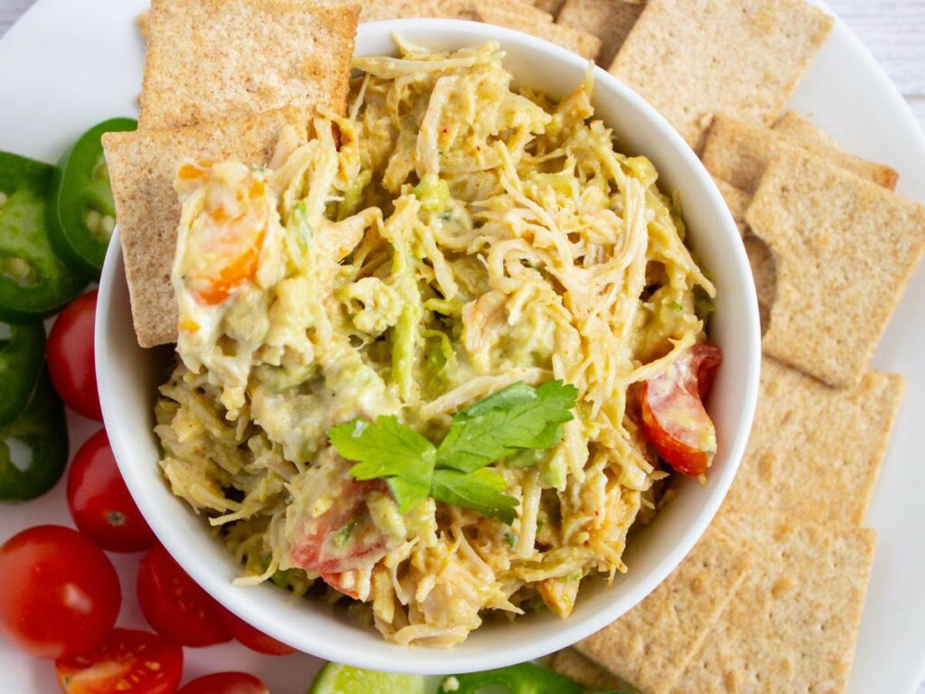 A bowl of healthy chicken salad with diced tomatoes and herbs.