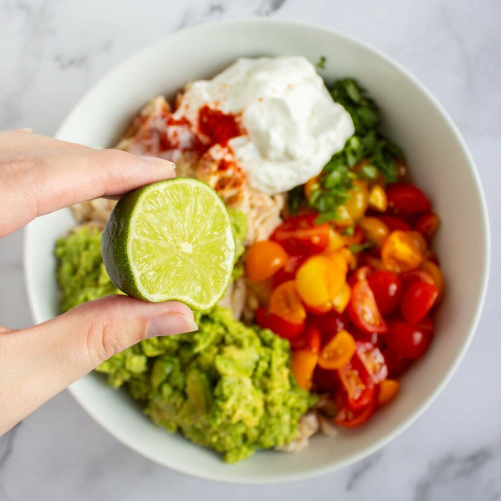 A hand holds half a lime above a bowl.