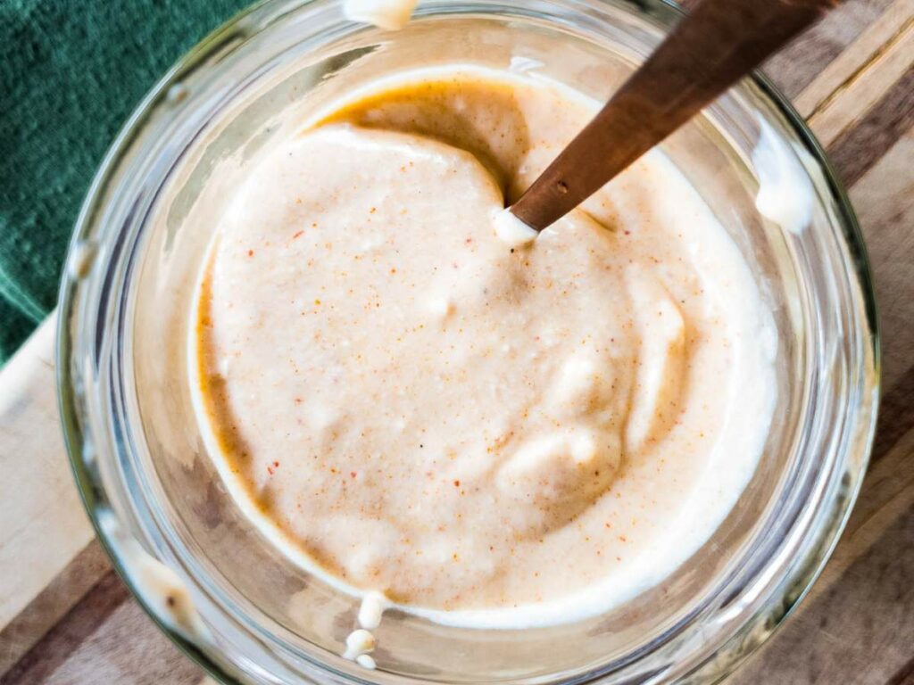 A glass bowl filled with horseradish sauce is shown with a spoon stirring in a swirl of sauce.
