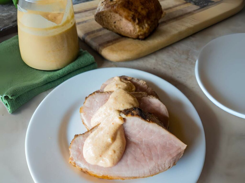 A plate of three sliced meat topped with creamy horseradish sauce and a glass bowl of same sauce next to it.