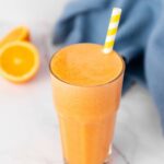 A tall glass of immunity boost juice with a yellow and white striped straw.