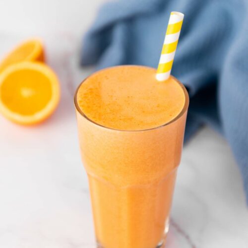 A tall glass of immunity boost juice with a yellow and white striped straw.