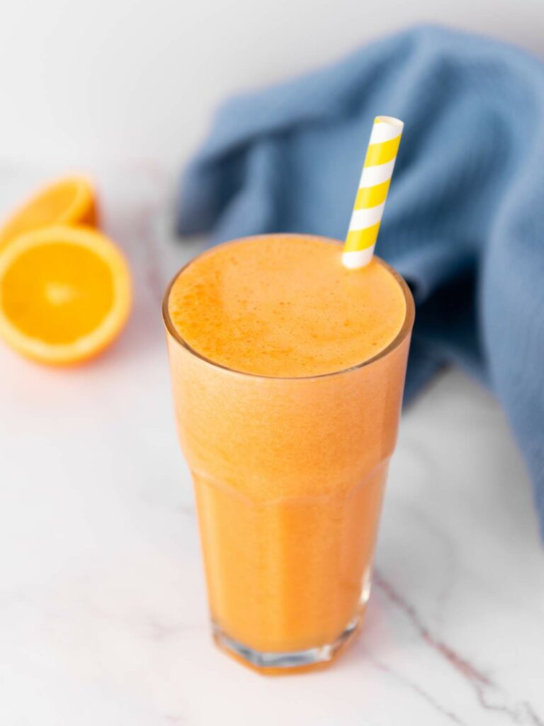 A tall glass of immunity boost juice with a yellow and white striped straw.