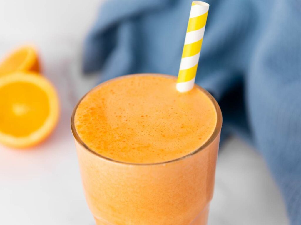 A glass of immunity boost juice with a yellow and white striped straw.