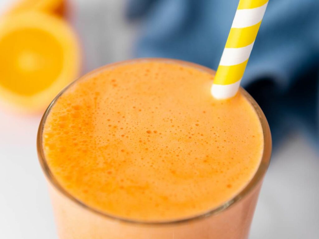 A close-up of an immunity boost juice in a glass with a yellow and white striped straw.