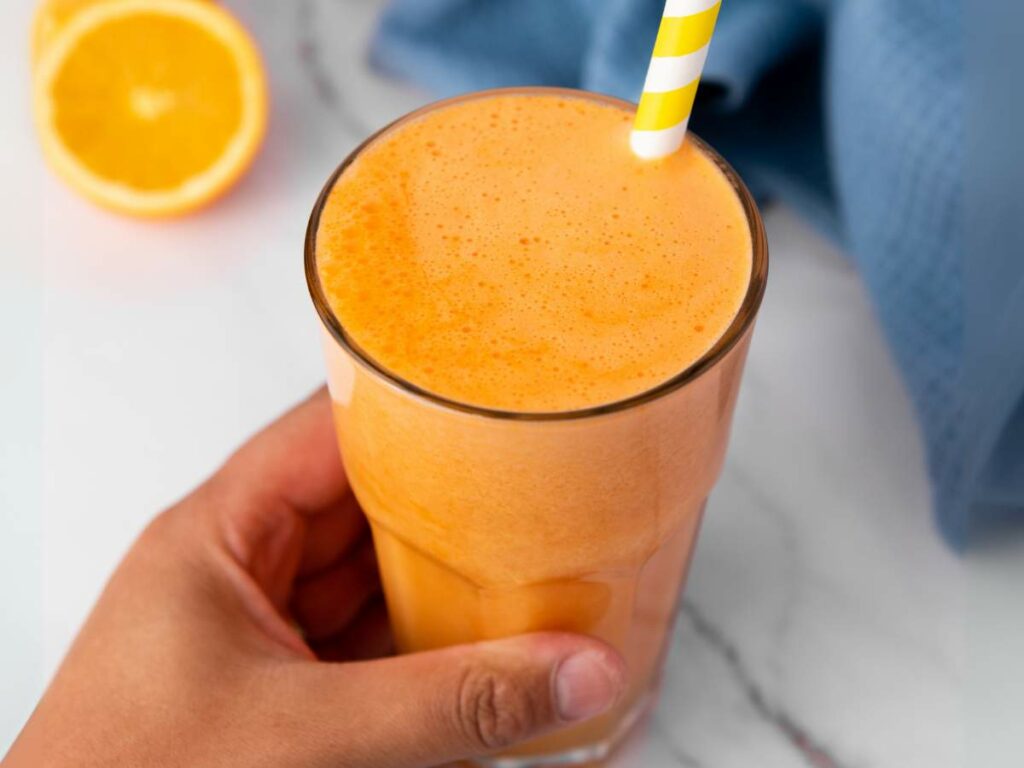 A hand holds a glass of immunity boost juice with a yellow and white striped straw.