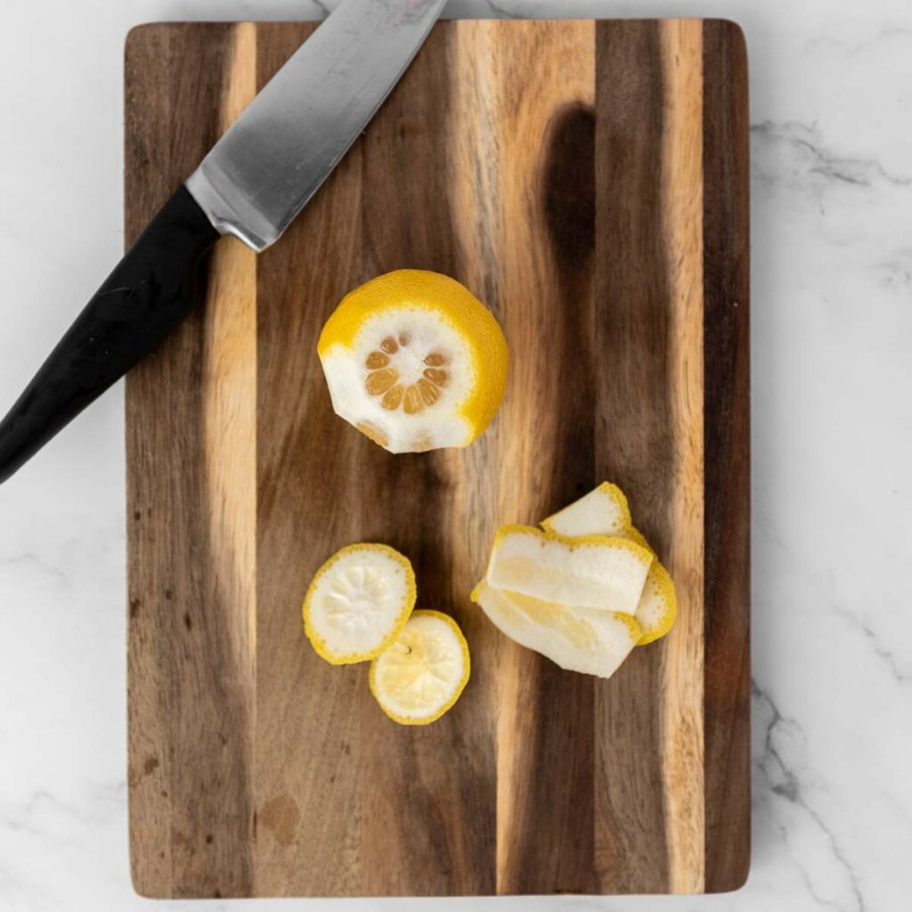 A partially peeled lemon with slices and peel sits on a wooden cutting board.