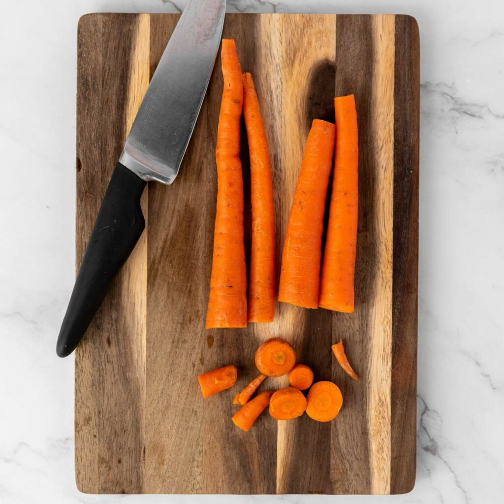 A kitchen knife and several whole and sliced carrots.