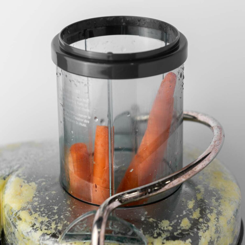 Two whole carrots inside a transparent container on top of a kitchen appliance.