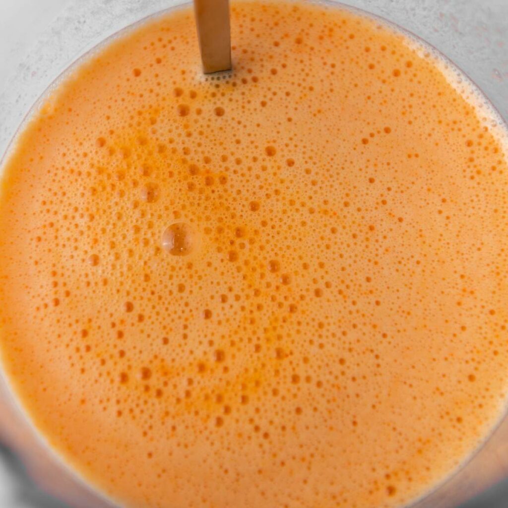 A close-up view of frothy orange juice in a transparent container.