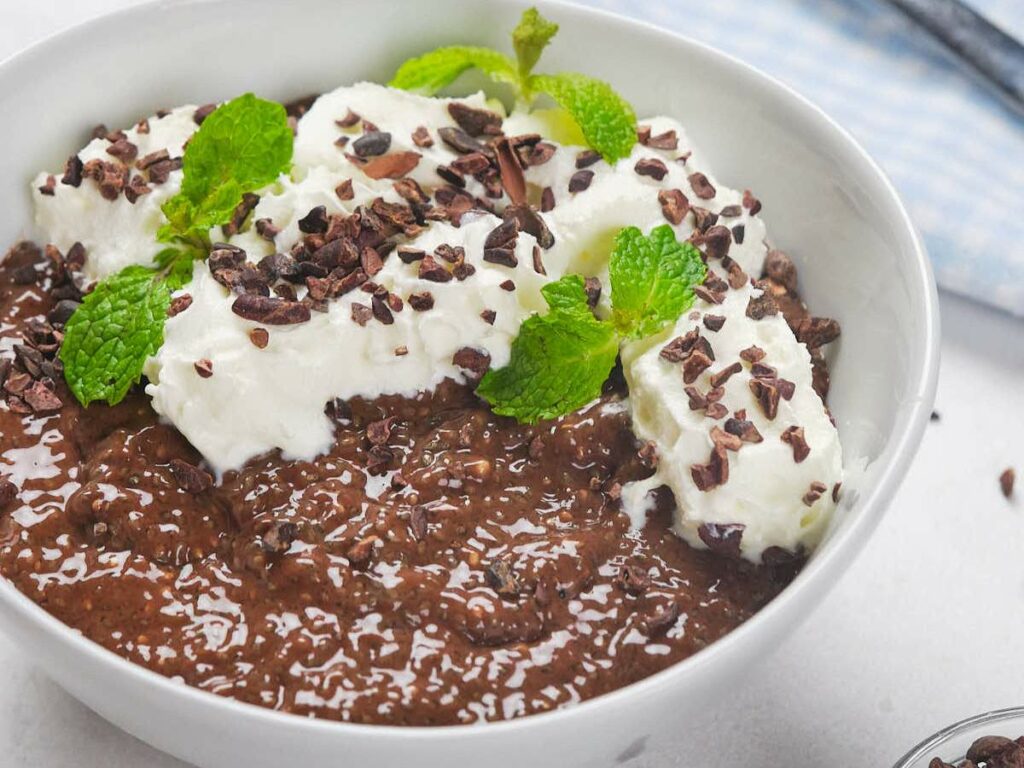 Chocolate chia pudding served in a white bowl, topped with cream.