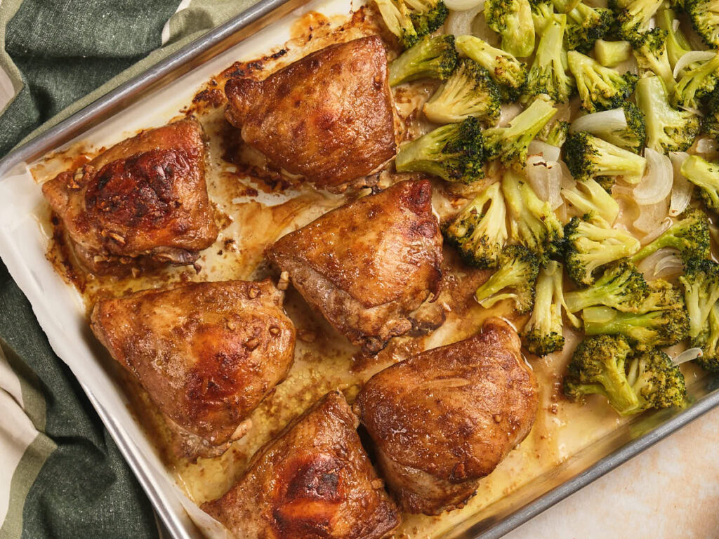 Sheet pan chicken thighs and chopped broccoli with onions on a sheet pan.