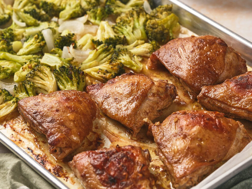 Sheet pan chicken thighs and broccoli florets with onions on a baking sheet.