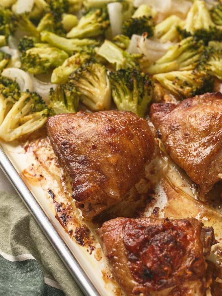 Sheet pan with sheet pan chicken thighs and broccoli florets.