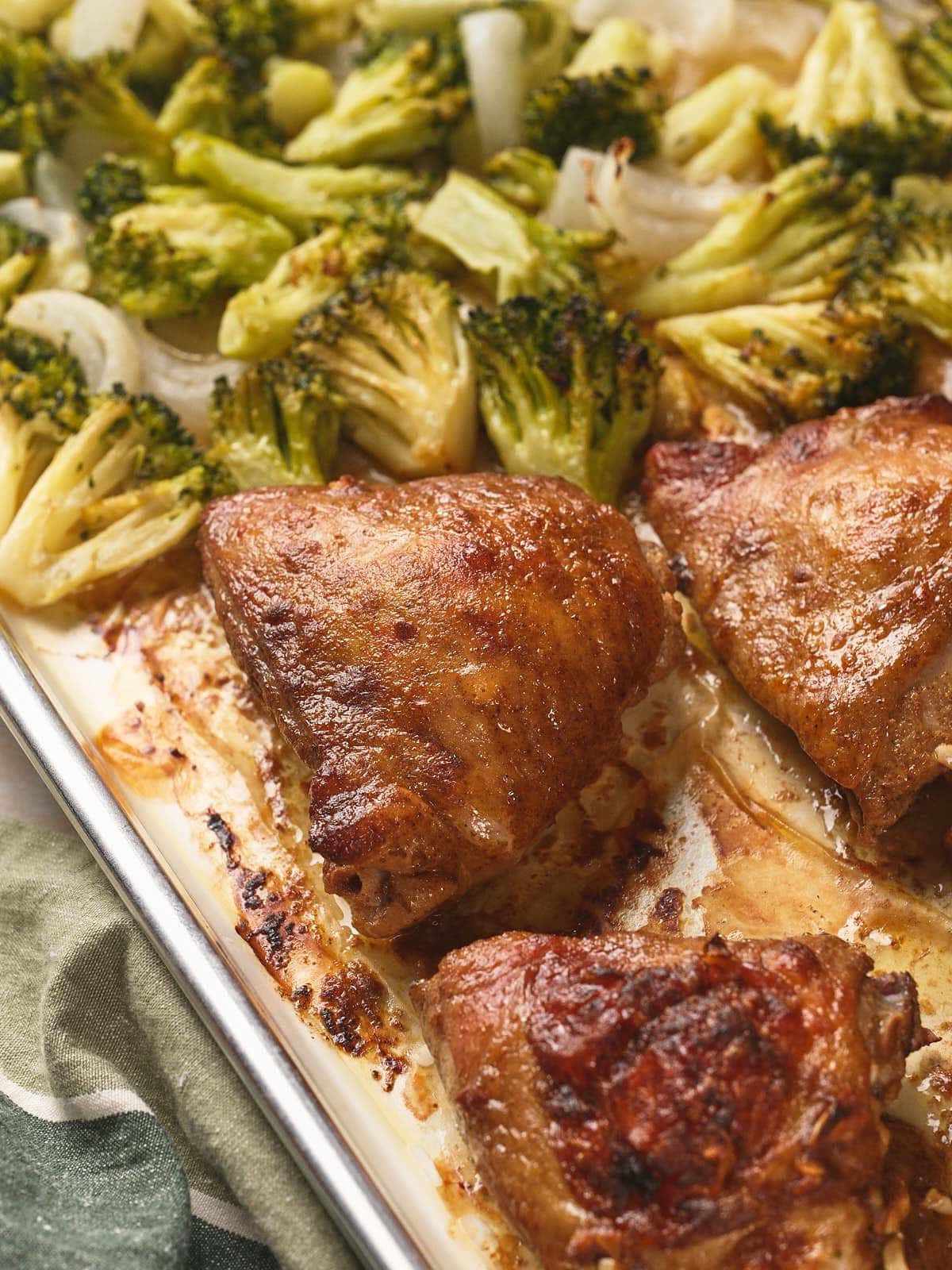 Sheet pan chicken thighs with broccoli florets and onions on a single baking sheet.
