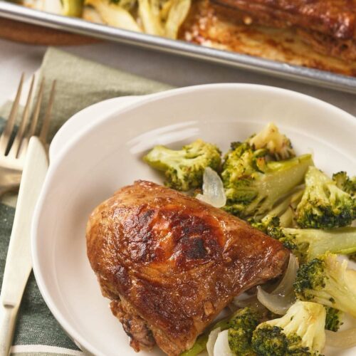 A plate with a piece of sheet pan chicken thighs and a side of cooked broccoli and onions.