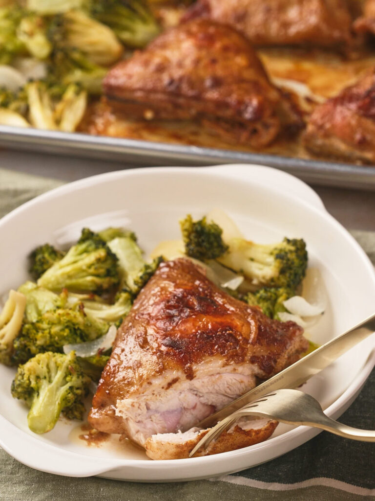 A plate with sheet pan chicken thighs, broccoli, and onion.