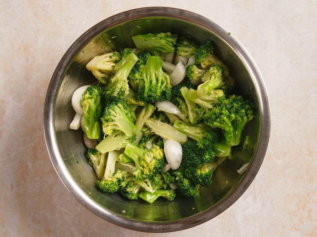 A stainless steel bowl filled with cooked broccoli florets and sliced onions.