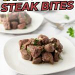 Two plates with garlic butter steak bites garnished with herbs, placed on a white surface with a fork and parsley in the background.