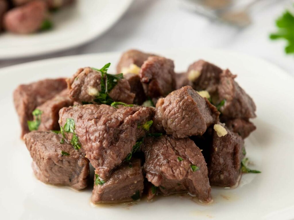 Chunks of steak bites garnished with chopped parsley.