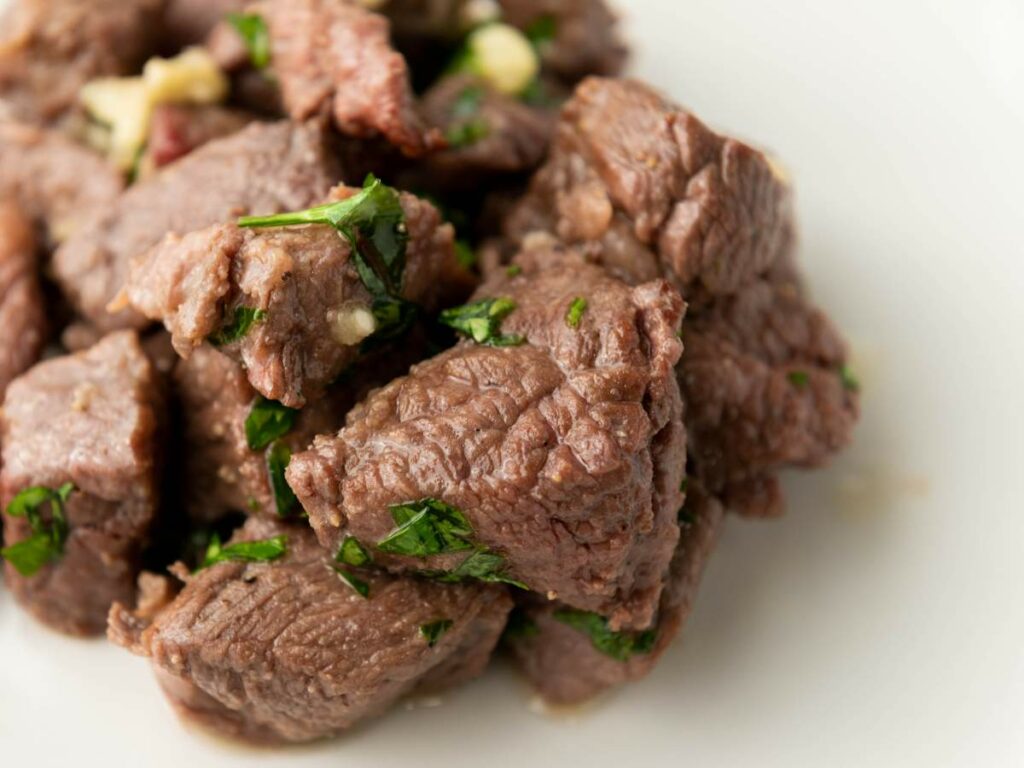 Close-up of cooked steak bites cubes garnished with chopped herbs.