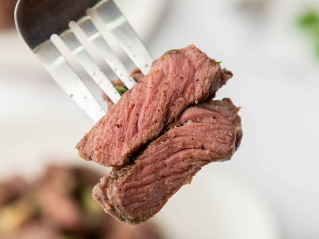A close-up of a fork holding two pieces of steak bites, showing a pink, medium-rare center.