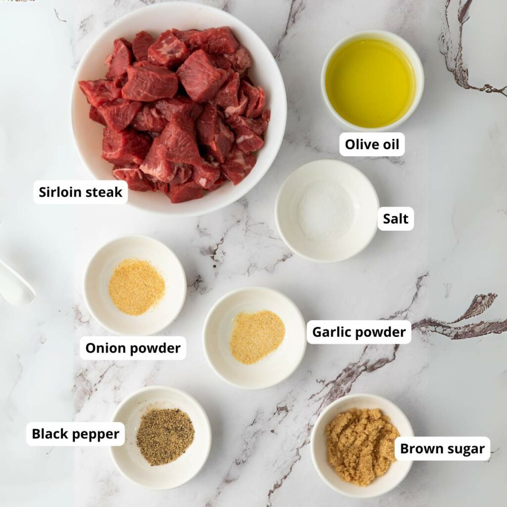 Bowls containing sirloin steak pieces, olive oil, salt, brown sugar, black pepper, onion powder, and garlic powder.