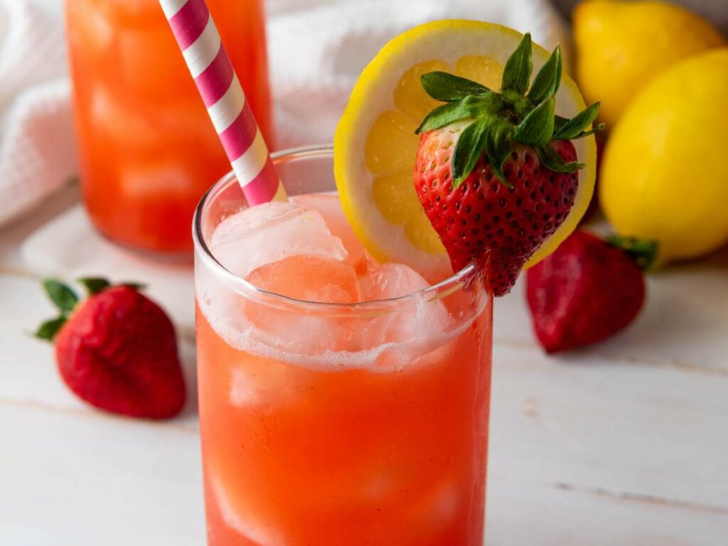 A strawberry lemonade garnished with a lemon slice and a strawberry, with a striped straw.