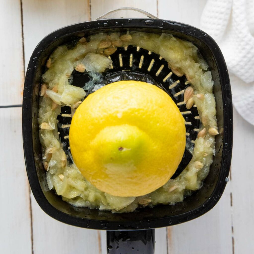 A lemon half is placed on a black citrus juicer on a white wooden surface.