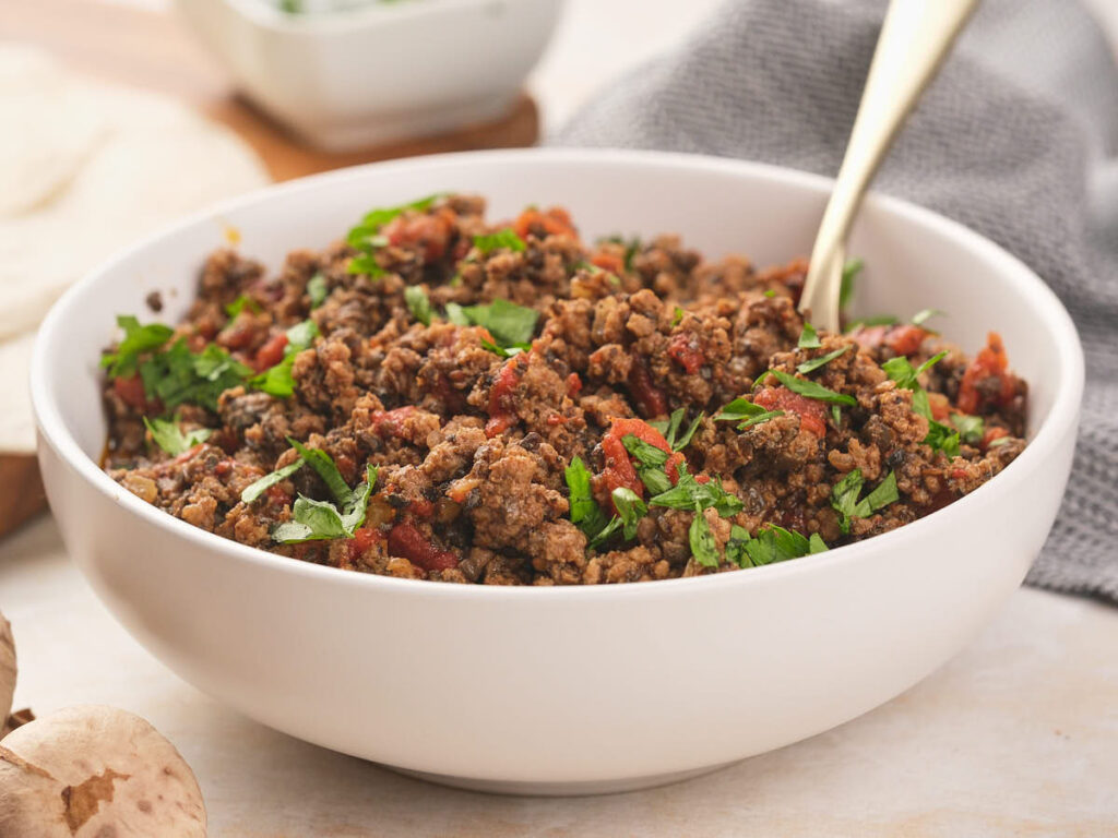 A bowl of seasoned ground beef garnished with fresh cilantro with a spoon inside.