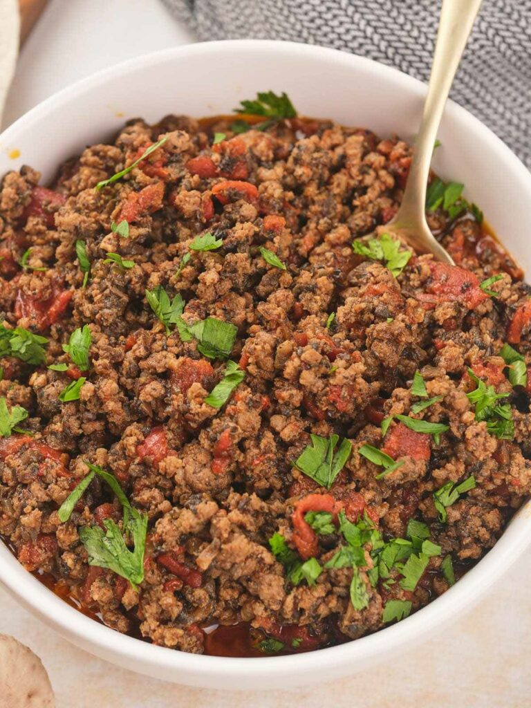 A white bowl of taco meat garnished with fresh cilantro with a spoon inside.