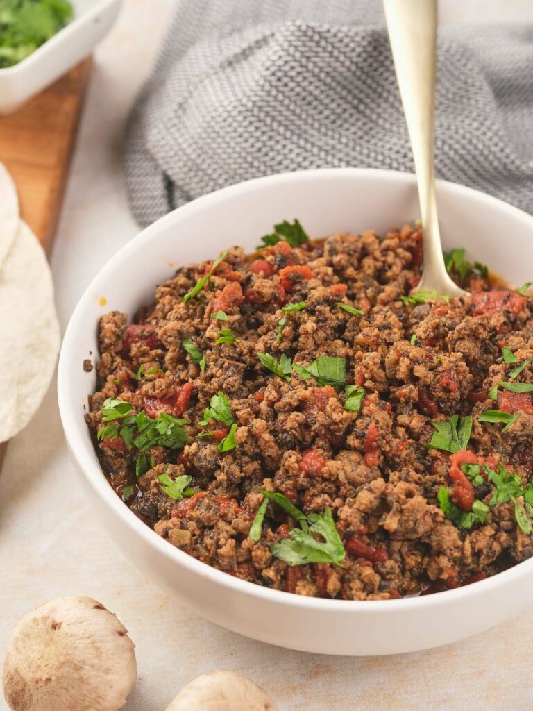 Mexican ground beef in a bowl with tortillas and mushrooms.