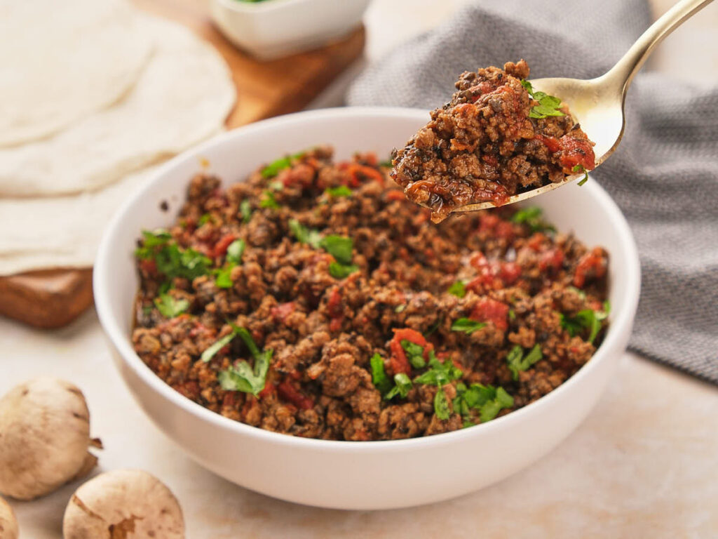 A spoonful of seasoned taco meat with cilantro being lifted from a bowl.