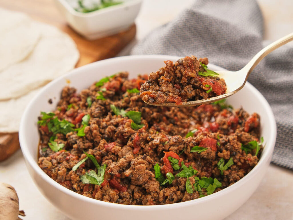 A taco meat and a spoonful of the same dish is being lifted in a white bowl.