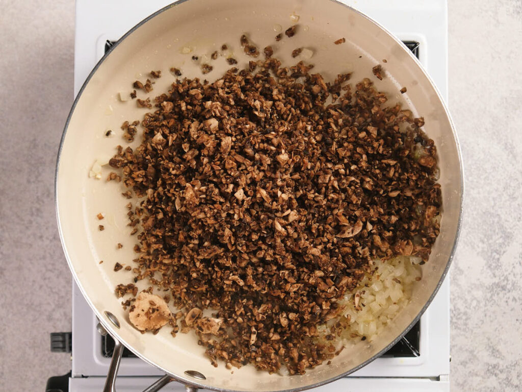 A white skillet filled with cooked mushrooms is cooking on a stovetop.