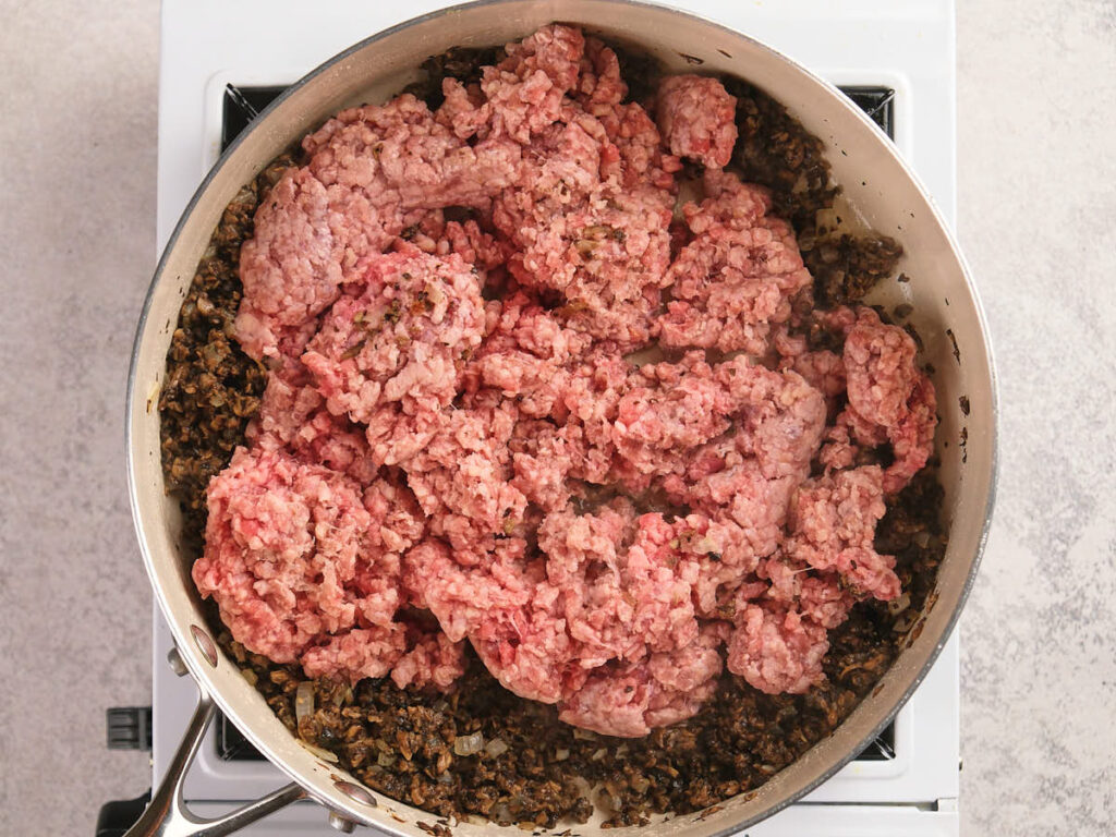 A skillet filled with sautéed mushrooms and ground beef in a stovetop.