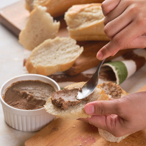 A person spreading beef liver pate on a slice of bread.