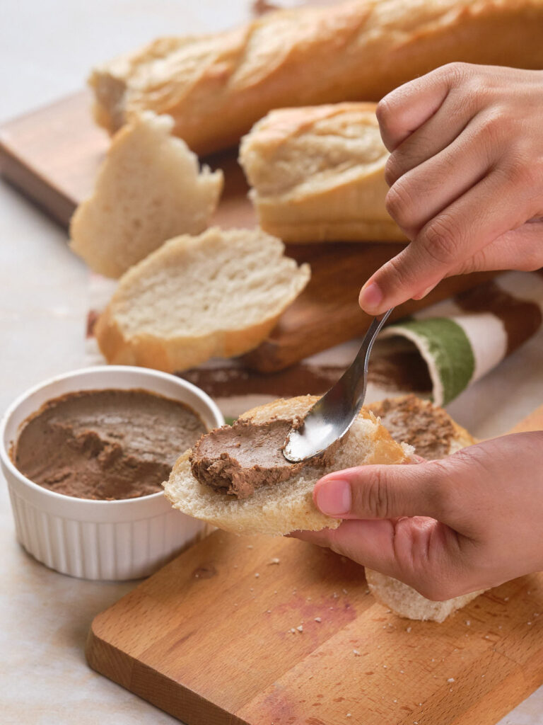 A person spreading beef liver pate on a slice of bread.