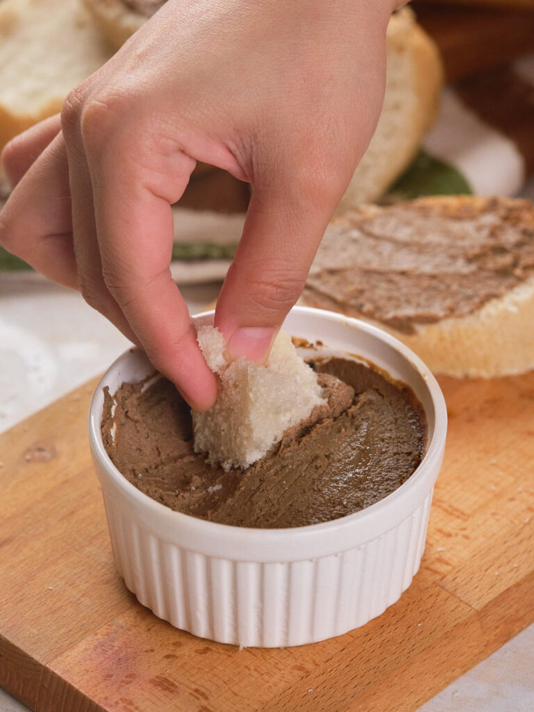 A hand dipping into a ramekin of liver pate.