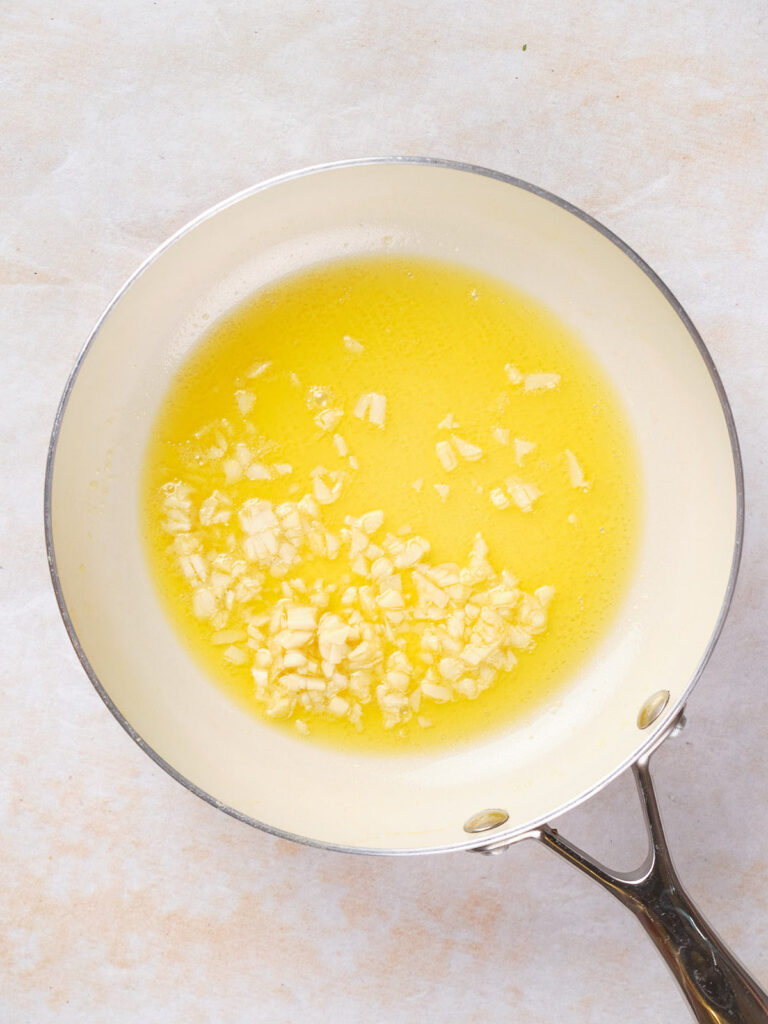 Minced galic and melted butter in a white skillet.