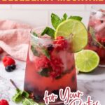 A glass of blueberry mocktail with ice, berries, mint, and a lime slice garnished on the rim.