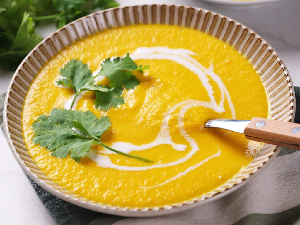 A creamy soup garnished with a swirl of coconut milk and fresh cilantro, with a spoon resting on the rim.