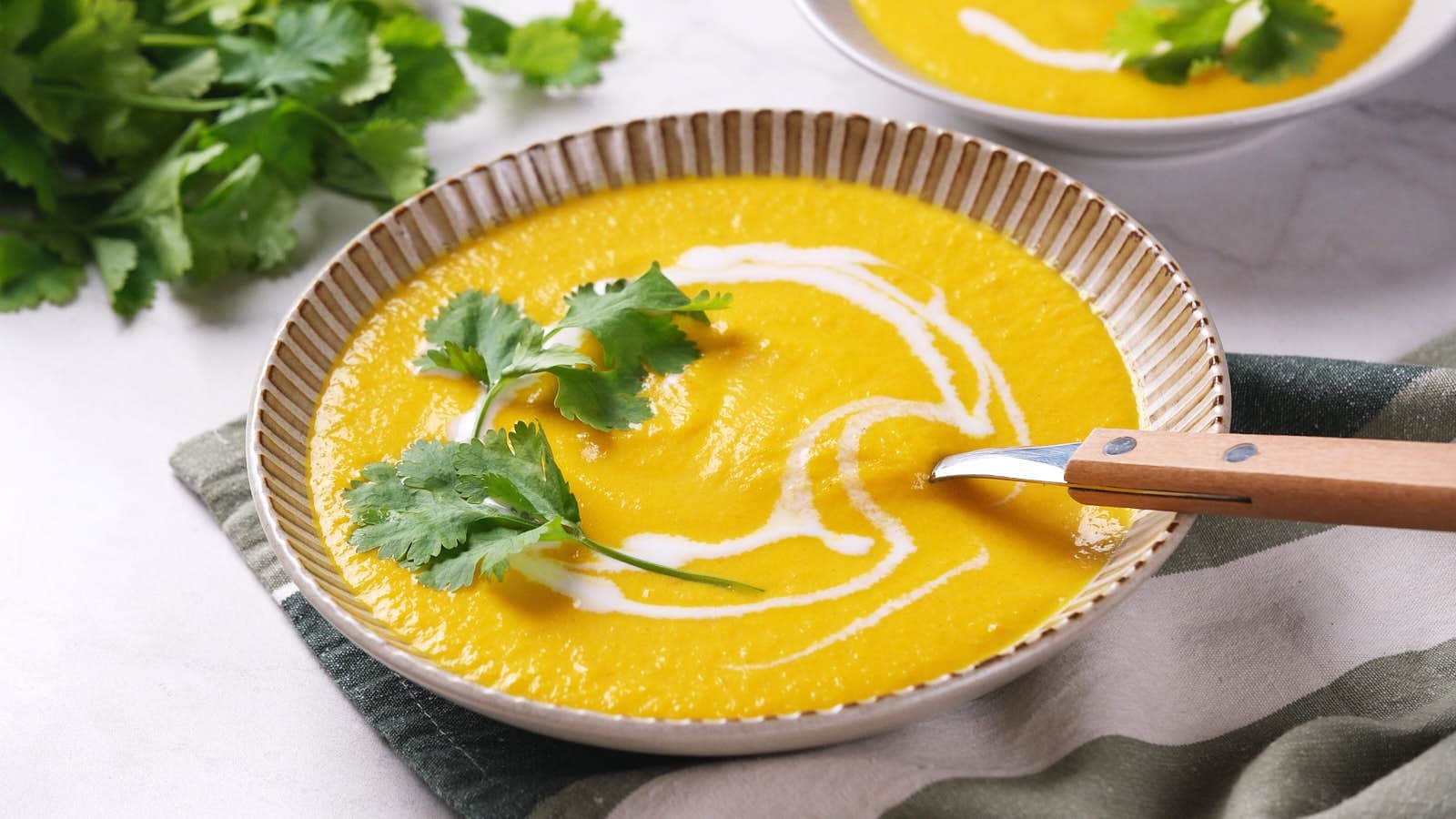 A bowl of yellow soup garnished with cilantro leaves and a swirl of coconut milk, with a spoon resting inside.