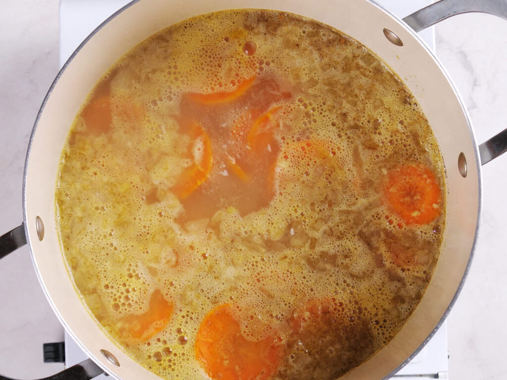 A pot of soup with visible sliced carrots and bubbling broth sits on a stovetop.